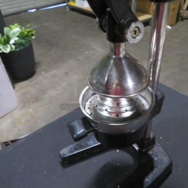 Stainless steel commercial juicer with manual lever, mounted on a sturdy black base, in used condition.