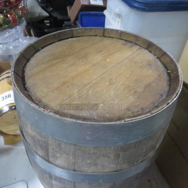 Wooden whiskey barrel with metal bands, showing vintage wear. Used condition, ideal for decor or repurposing projects.
