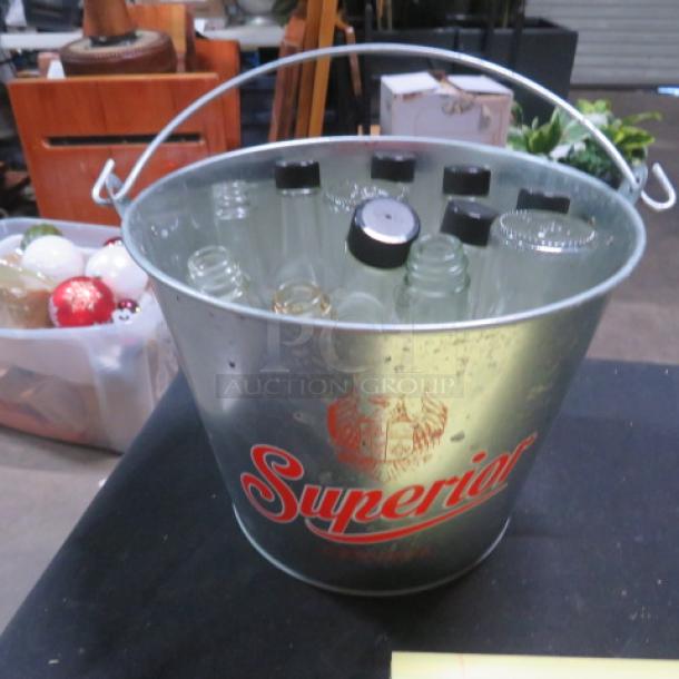 Metal beer bucket with "Superior" logo, containing multiple empty glass bottles, in good condition. Sturdy handle.