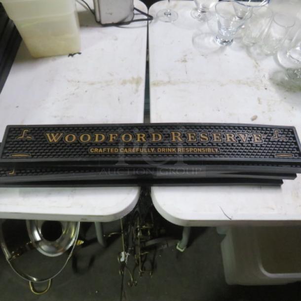 Woodford Reserve bar mat with gold lettering, reads "Crafted Carefully, Drink Responsibly." Black, textured surface. Good condition.