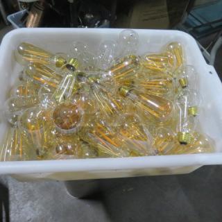 Container of vintage-style clear filament light bulbs, mix of sizes, in good condition. Ideal for collectors or decorators.