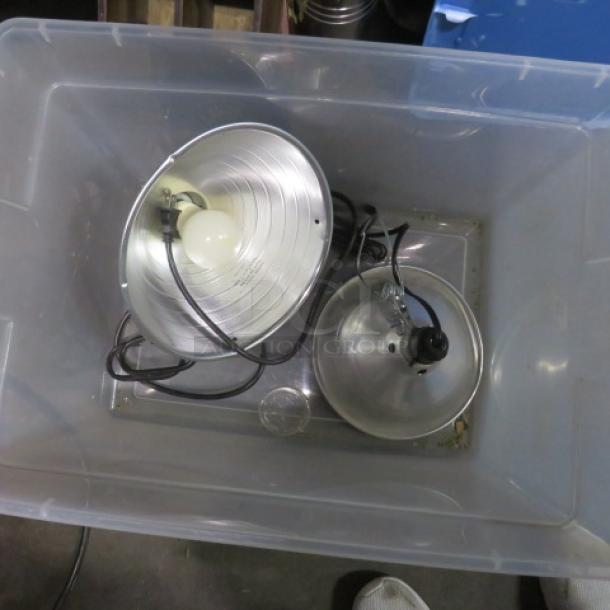 Two metal heat lamps in a plastic bin; one with a bulb, cords visible. Good condition. Model: 2XBID.