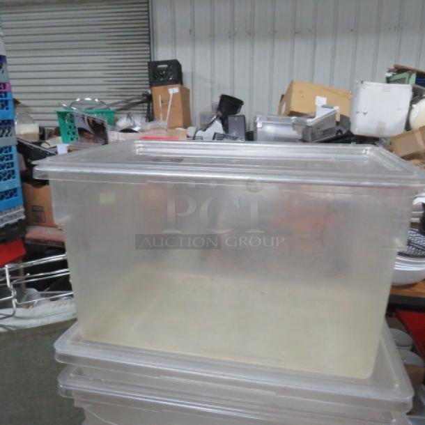22-gallon transparent food storage container with lid, in good condition, on a stack of similar containers in a warehouse.