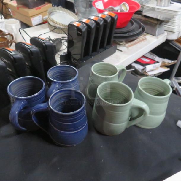 Assorted color coffee mugs, set of six: 3 green and 3 blue, ceramic, displayed on a table. Condition appears good.