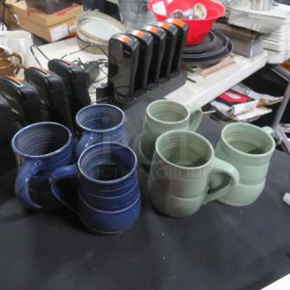 Assorted color coffee mugs, set of six: 3 green and 3 blue, ceramic, displayed on a table. Condition appears good.