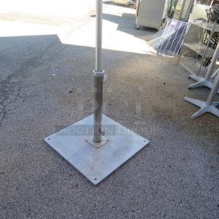 Stainless steel umbrella base with square plate and central pole holder, suitable for outdoor use, in used condition.