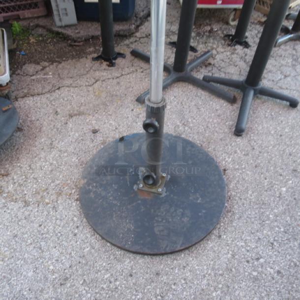 Black metal umbrella base, round design, visible scuffs, smooth finish, outdoor use, suitable for stability.