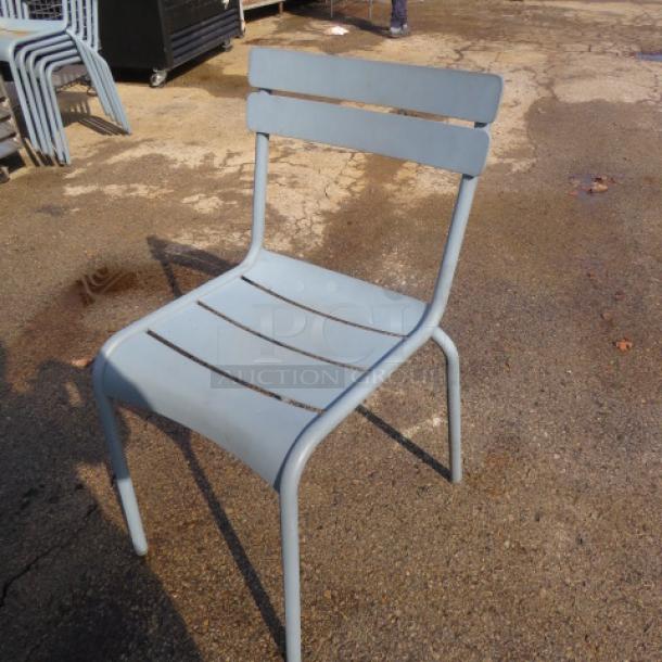 Aluminum patio chair, light blue, slatted design, sturdy construction. Slight wear, suitable for outdoor use.