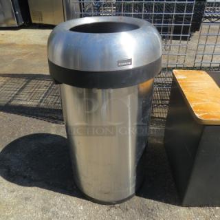 Simple Human round trash can with lid, stainless steel, noticeable wear, brand label visible, outdoor setting.