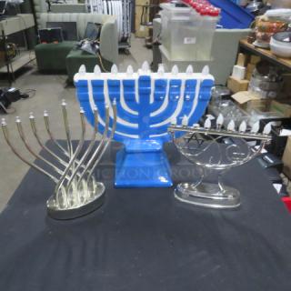 Assorted menorahs including a large blue electric menorah and two silver menorahs, in good condition, on display table.