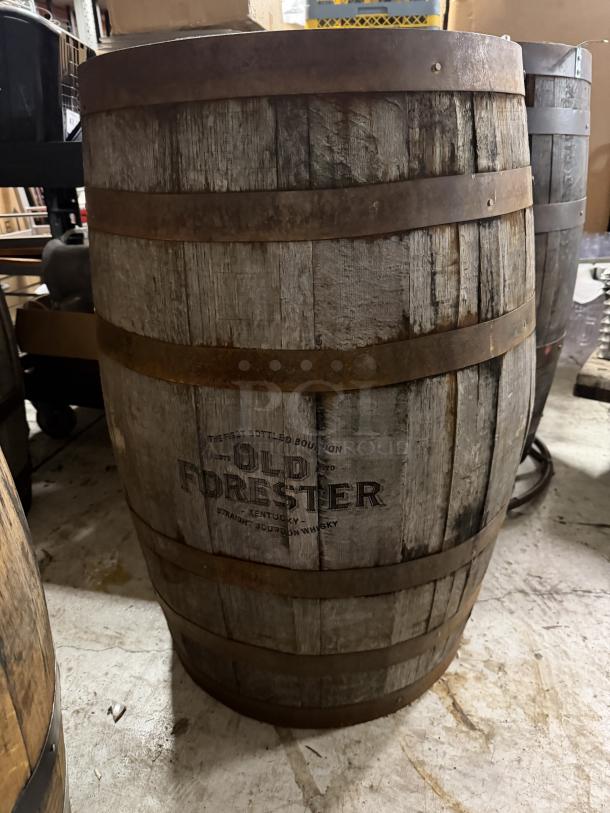 Old Forester whiskey barrel, worn wood and rusted metal bands, branded logo visible, used for bourbon aging.