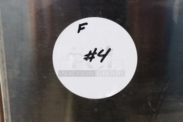 Round white label with handwritten text "F #4" on stainless steel surface of coffee brewer. Possible minor scratches/dents.