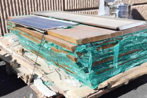 Stack of 11 wood table tops, top piece with visible cracks, wrapped in green packing material. Auction lot includes 11 pieces.