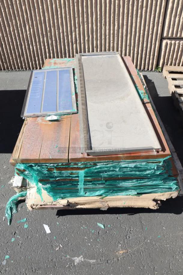 Stack of 11 wood table tops, top piece has visible cracks, wrapped in green wrap, ready for auction.
