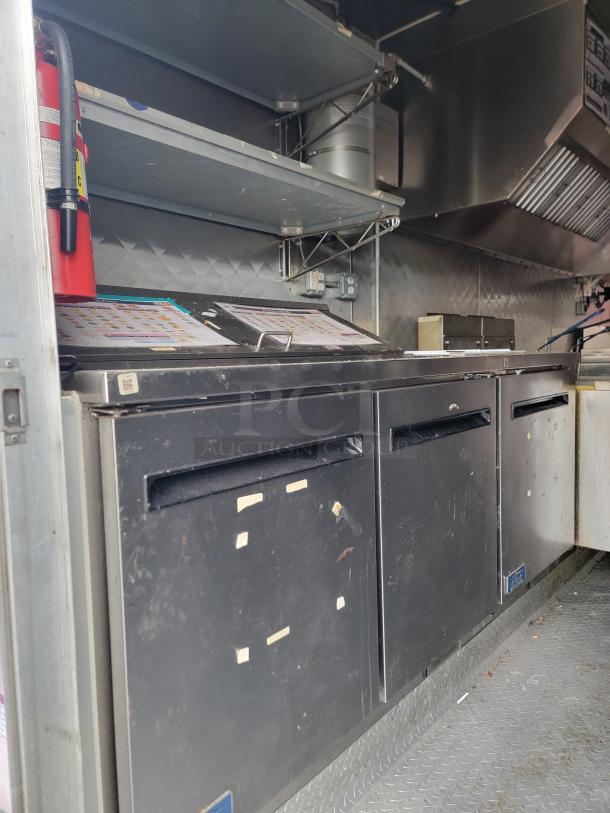 2021 16' Quality mobile kitchen trailer interior featuring Arctic Air undercounter refrigerators, fire extinguisher, shelves, and exhaust hood.