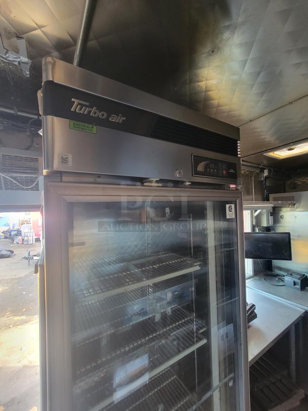 Turbo Air glass display cooler inside a 2020 Quality 16' mobile kitchen trailer. Features visible shelving and stainless steel walls.