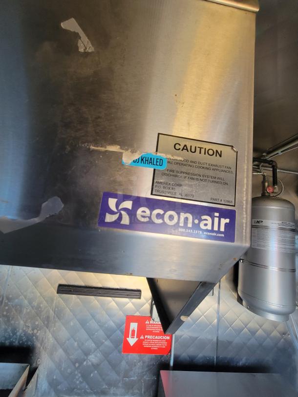 The interior of a 2020 Quality 16' mobile kitchen showing an econo-air hood with caution labels and fire suppression system.
