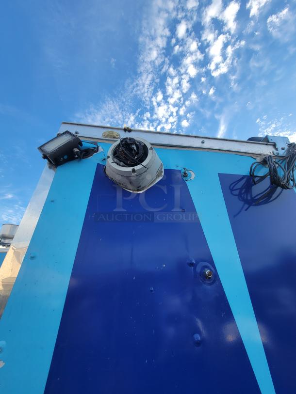 2019 Quality 24' food trailer exterior with blue paneling. Features visible security camera and lighting fixtures.