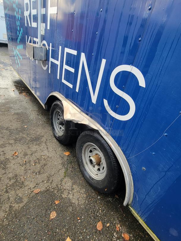 2019 Quality 24' food trailer, blue exterior, twin axles. Side branding "REEF Kitchens." Visible wheel and part of the logo.
