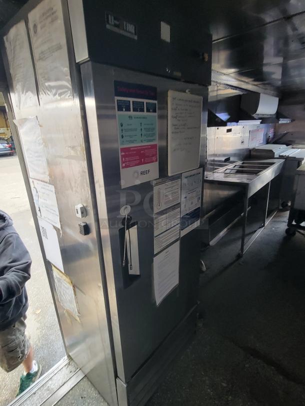 2019 Quality 24' food trailer interior with stainless steel fridge. Visible safety and sanitary labels. Fully equipped kitchen.