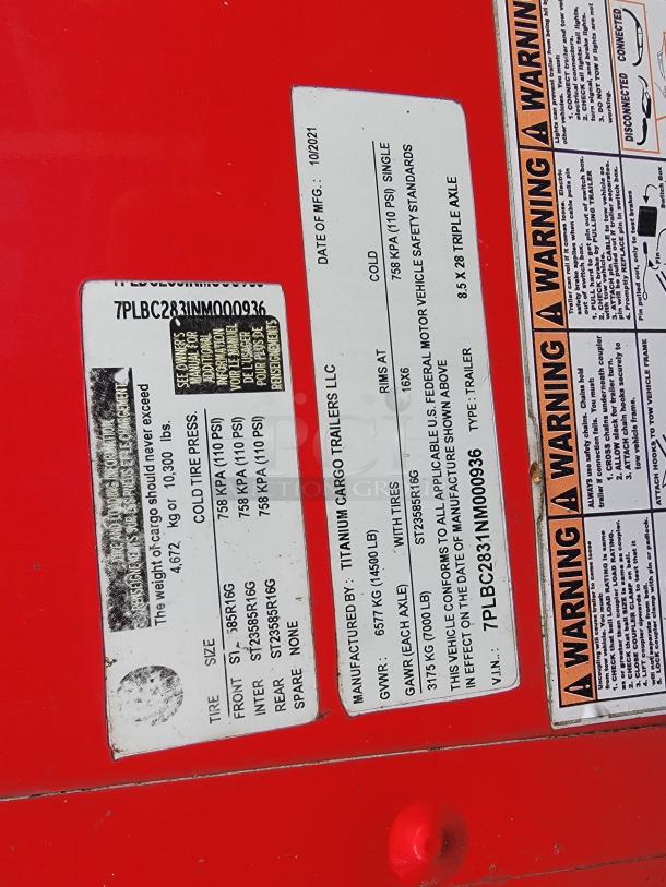 Metal tag on red background showing manufacturer info and VIN for 2021 Titanium Cargo Trailer.