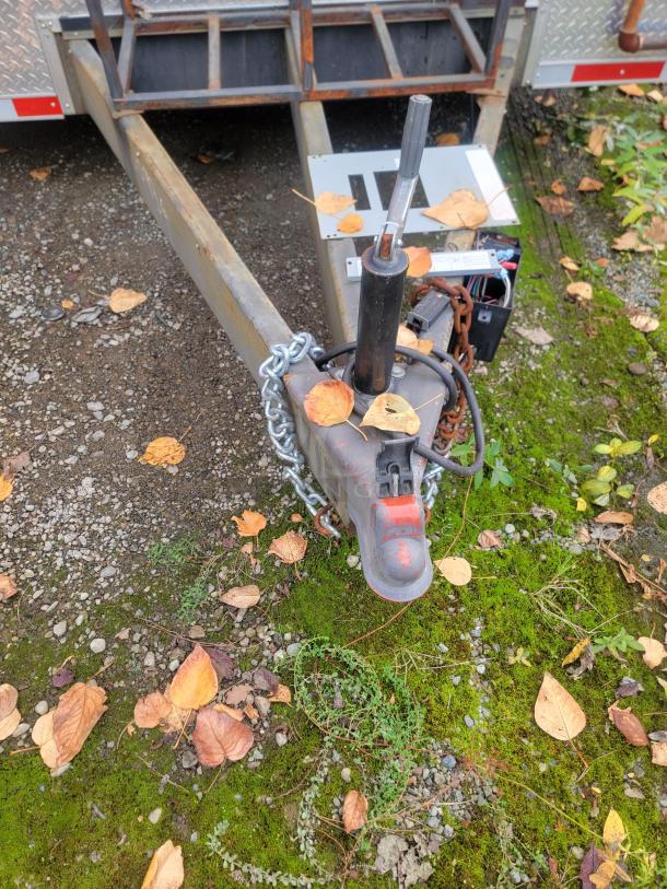 Trailer hitch of 2021 28' Wendy's Mobile Ghost Kitchen. Rusty metal frame with chains and fallen leaves on gravel.