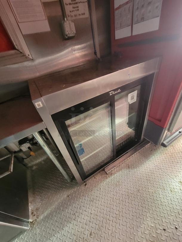 Inside of a Wendy's Ghost Kitchen trailer with a True commercial refrigerator. Metal flooring and stainless steel surfaces visible.