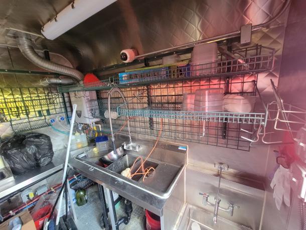 2021 Quality Kitchens 24' mobile food trailer interior; features stainless steel sinks, wire shelving, and sanitation station.