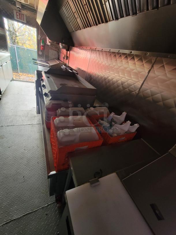 2021 24' Quality Kitchens mobile food trailer interior with gas griddle, Imperial fryers, Econ-Air exhaust hood, and storage crates.