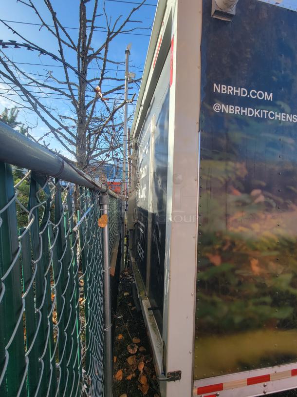 24' Quality food trailer parked in a narrow space, featuring exterior graphics, website URL, and social media handle.