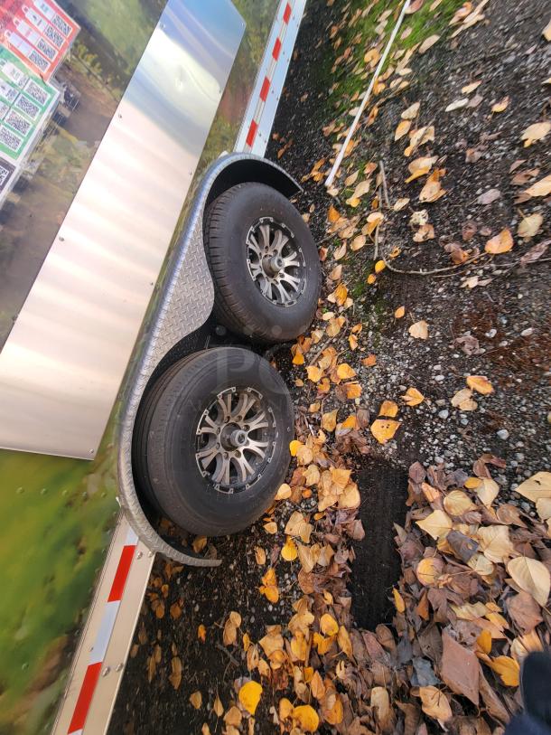 2021 Quality 24' tandem axle food trailer with chrome wheels, surrounded by autumn leaves, exterior view.