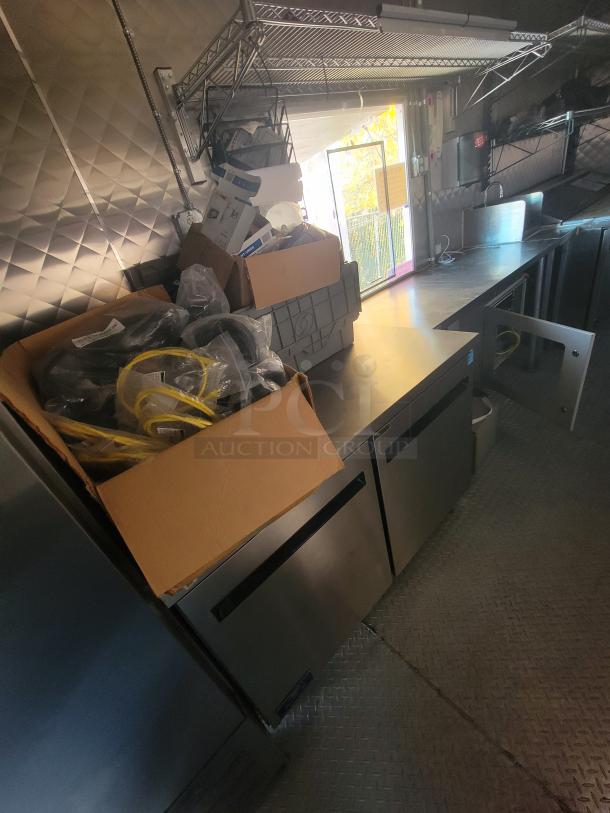 24' food trailer interior with stainless steel surfaces. Features Econ-Air exhaust hood, Arctic Air refrigeration units, and shelving.