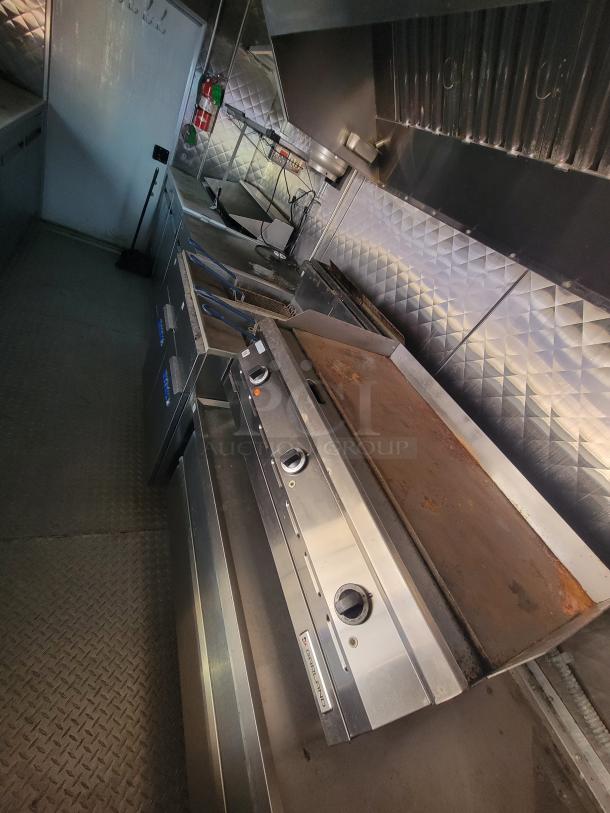 Interior of a 2021 Quality 24' food trailer, featuring stainless steel build, gas griddle, deep fryers, and exhaust hood.