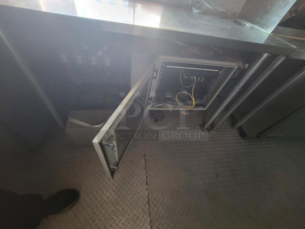 Interior view of 2021 Quality 24' food trailer showing the stainless steel counter, open cupboard with wiring, and diamond-plate flooring.