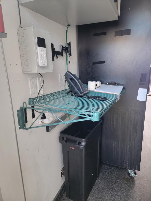 Mobile retail trailer interior with IT/security setup. Features chrome wire shelving, phone, power outlets, and sanitation station.