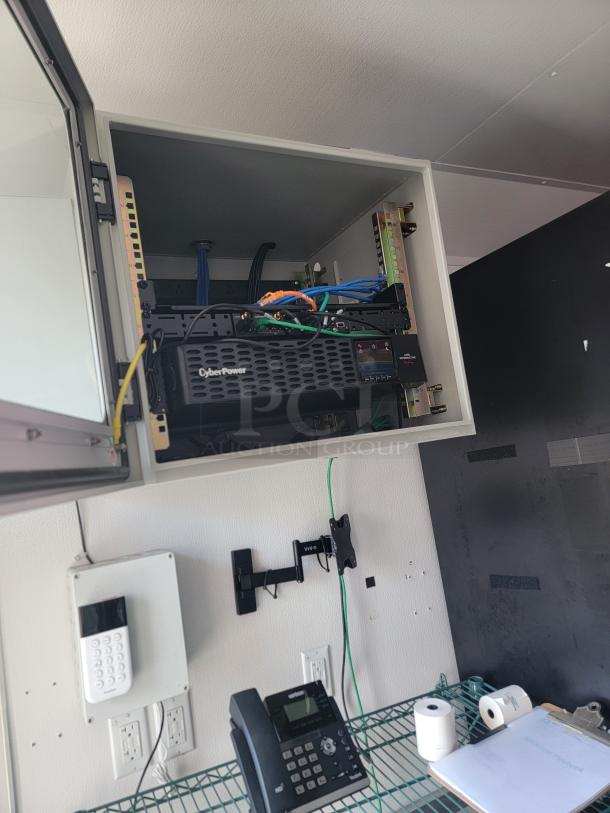 Mobile retail trailer interior with IT/security setup. Features a CyberPower UPS, network rack, security keypad, phone, and shelving. Ideal for a high-volume business.