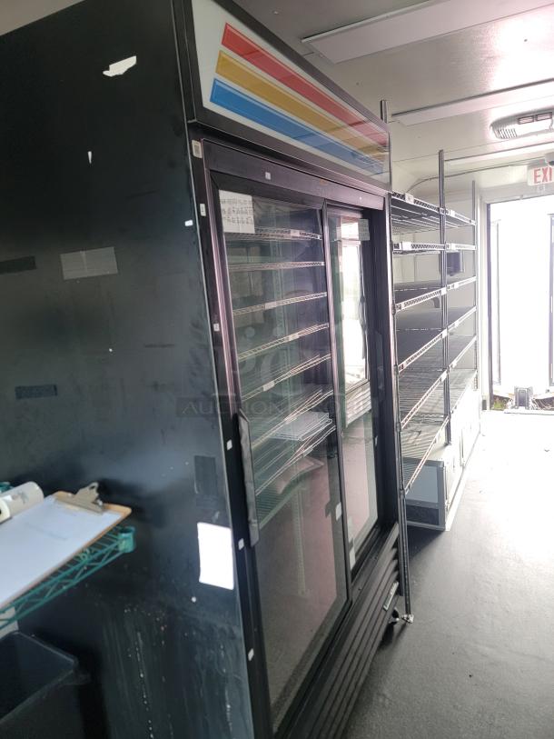 SDG mobile retail trailer interior with full-length chrome wire shelving, glass-front refrigeration unit, and IT/security setup.