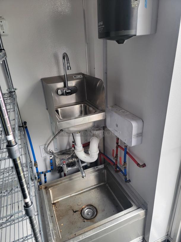 Stainless steel hand sink with running water, part of SDG mobile retail trailer. Features hot/cold pipes and wiring setup.