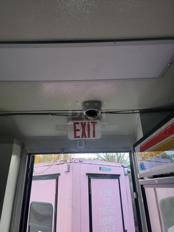 Interior view of mobile retail trailer with exit sign, security camera, and visible pink exterior of another unit outside.