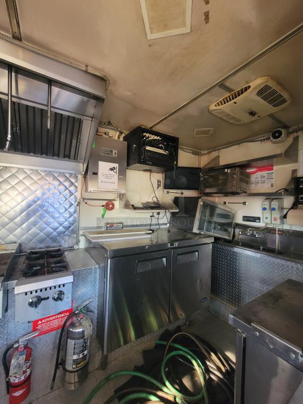 Mobile kitchen interior of a 2018 Southwest Trailer Mfg. 14-foot concession trailer. Features commercial appliances, stainless steel counter, refrigeration unit, and cooking equipment. Suitable for food business startups. Clean and well-maintained.