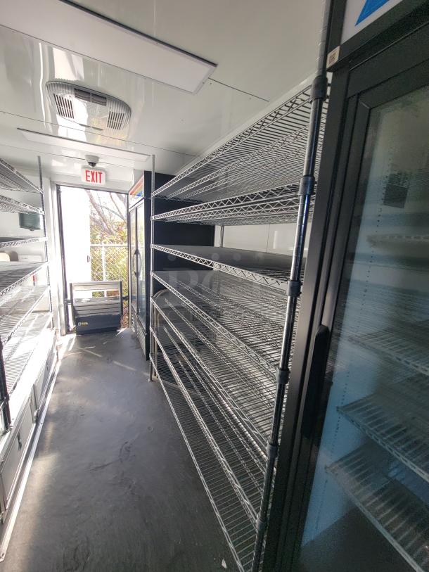Interior of a 2021 SDG 20-foot mobile retail trailer with shelving, commercial refrigeration units, and exit door.