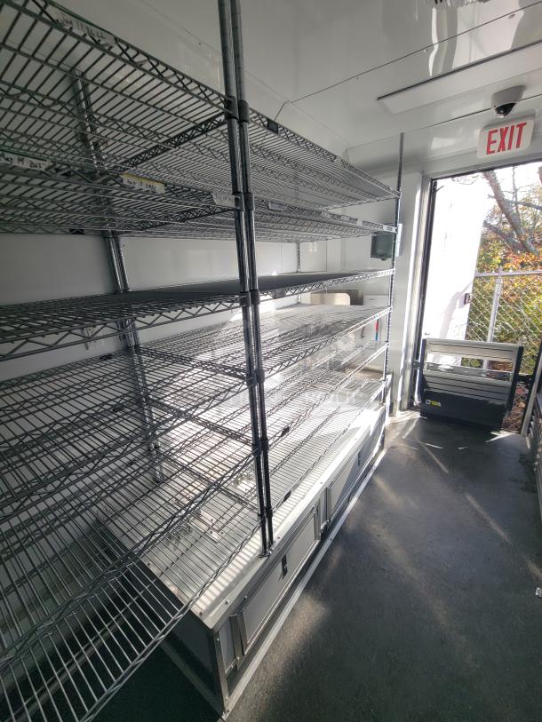 Interior of 2021 SDG 20' mobile provisions trailer showing metal shelving, pos area, counter space, and sink.