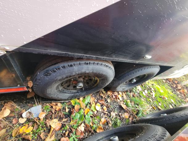 Black dual-axle wheels of a 2021 SDG 20' mobile market trailer on a damp, leafy ground, showcasing its robust chassis.