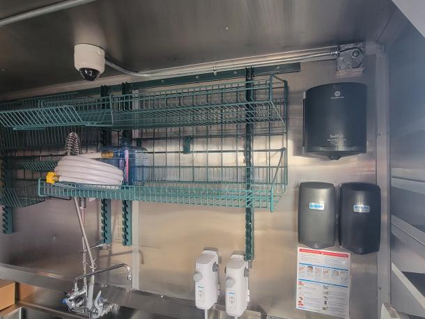 Interior of a never-used 2022 Rock Solid Cargo 28' ghost kitchen trailer. Features wire shelving, industrial sink, Ecolab dispensers, and Georgia-Pacific SofPull paper towel dispenser.