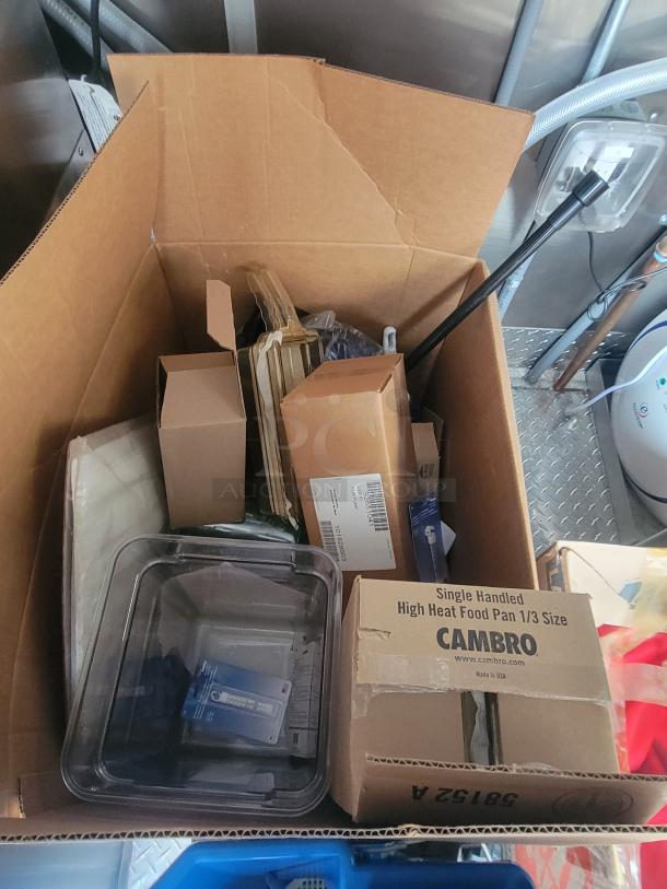 Cardboard boxes filled with various kitchen supplies inside a ghost kitchen trailer, featuring a Cambro High Heat Food Pan box.