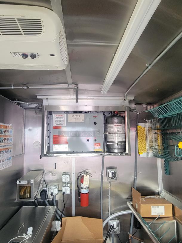 Interior of a 2022 Rock Solid Cargo 28' ghost kitchen trailer. Features include electrical panel, fire extinguisher, wiring, and stainless steel surfaces. New condition, never used.