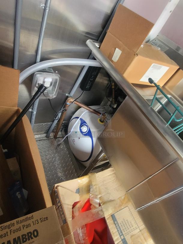 Interior view of never-used Rock Solid Cargo 28' trailer showing industrial plumbing and equipment setup surrounded by packaging and boxes.