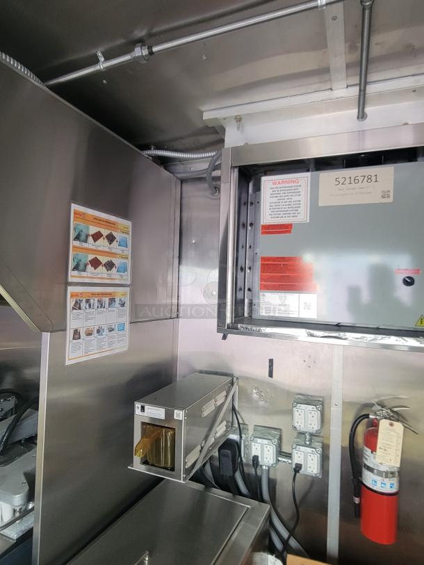 Interior of a never-used 2022 Rock Solid Cargo ghost kitchen trailer featuring stainless steel walls, wiring for three-phase power, a fire extinguisher, and instructional and warning labels.