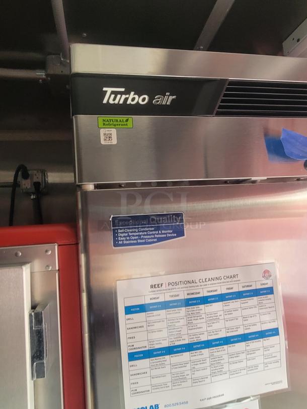 Turbo Air refrigerator in a 2022 Rock Solid Cargo ghost kitchen trailer. Features stainless steel, natural refrigerant label, and cleaning chart.