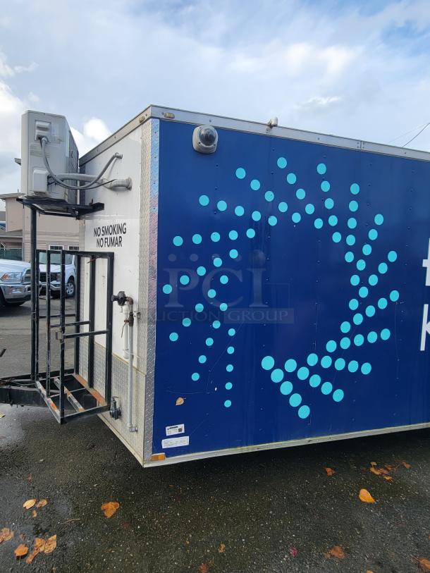 Quality Cargo Model 24 trailer, blue exterior with geometric pattern, external air conditioning unit, "No Smoking" sign visible.